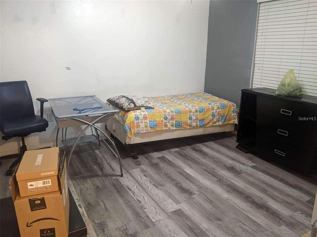 A bedroom features a single bed, a glass desk, a dark dresser, and wood-look flooring — 4000 SW 23RD STREET UNIT 4-103 #3, GAINESVILLE, FL