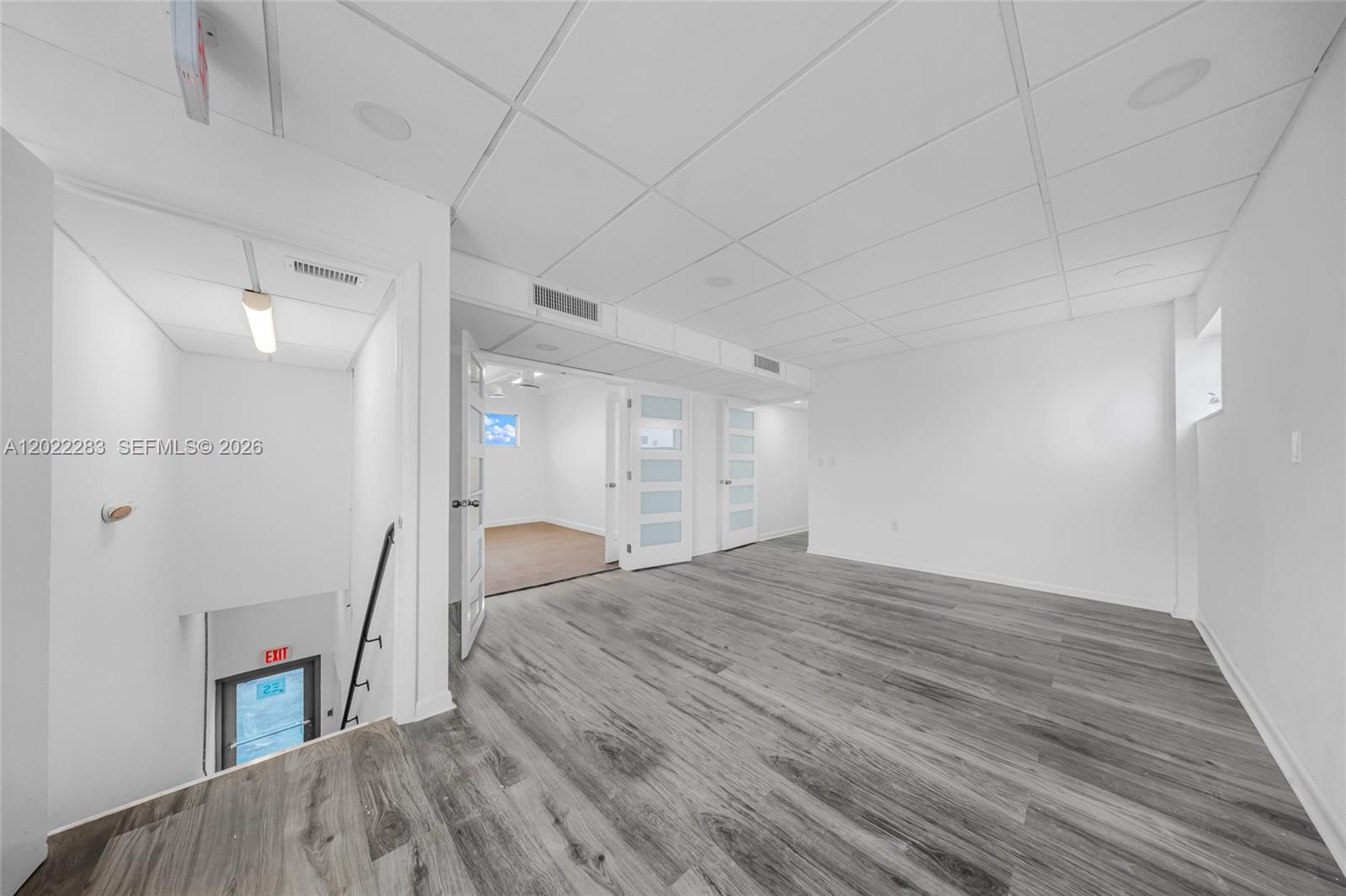 A bright room with gray wood-look flooring, a drop ceiling, and an adjacent staircase — 7550 W 2nd Ct, Hialeah FL 33014, HIALEAH, FL