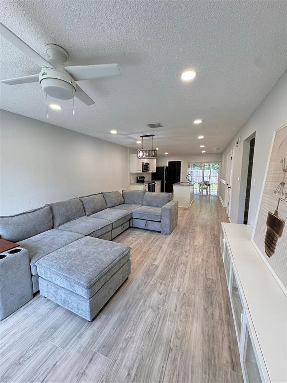 A living room with light wood-look flooring flows into an open kitchen with white cabinets — 8043 PUFFIN DRIVE, ORLANDO, FL