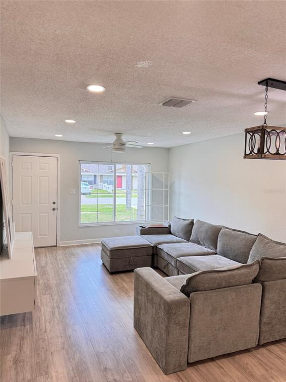 A living room features a gray sectional sofa, light wood flooring, and a ceiling fan — 8043 PUFFIN DRIVE, ORLANDO, FL