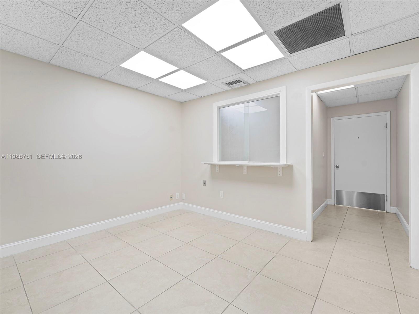 A small office room features beige tile flooring, a drop ceiling, and a service window — 1312 SW 27th Ave, Miami FL 33145, MIAMI, FL