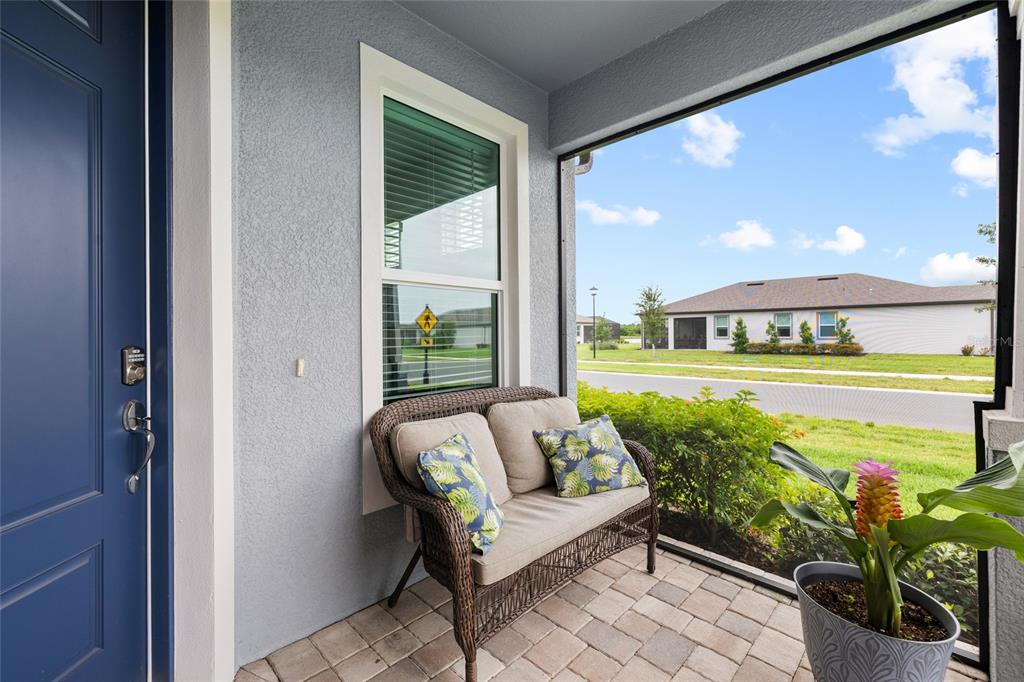 A covered patio features a wicker loveseat, a potted plant, and a view of the neighborhood — 9454 BALLASTER POINTE LOOP, PARRISH, FL
