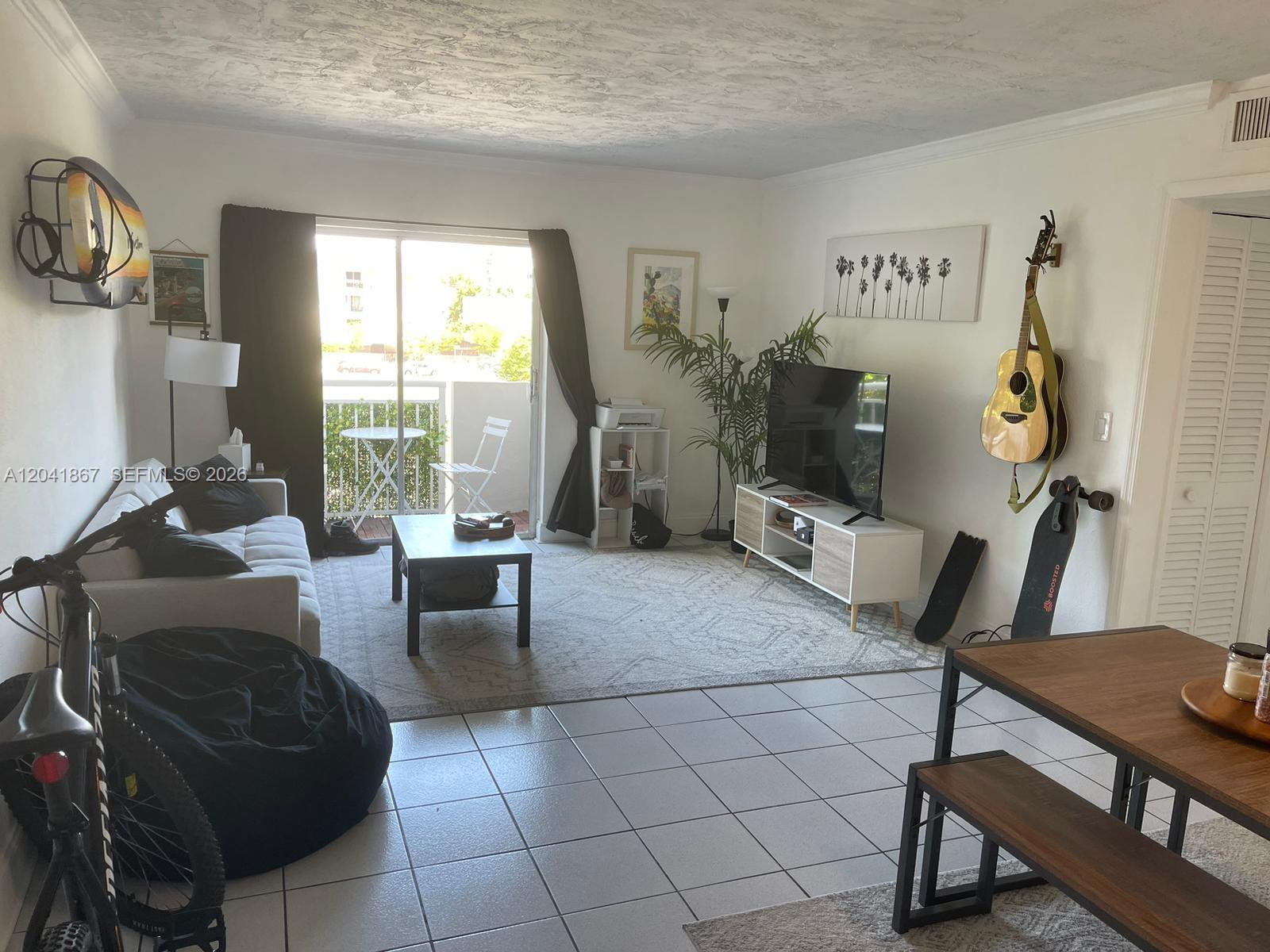 A living room features a sofa, television, coffee table, and a balcony with outdoor seating — 130 Mendoza Ave # 33, Coral Gables FL 33134, CORAL GABLES, FL