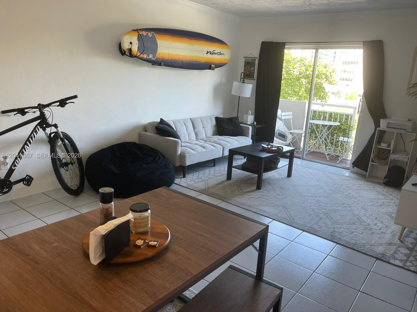 A living room features a surfboard on the wall, a sofa, and a dining table — 130 Mendoza Ave # 33, Coral Gables FL 33134, CORAL GABLES, FL