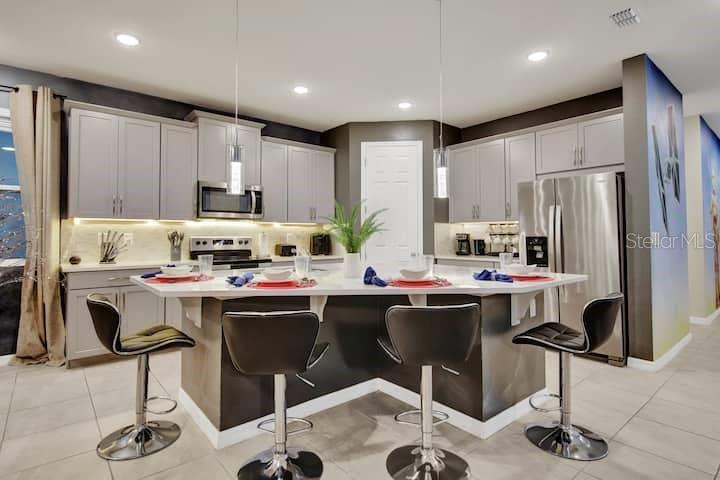 A modern kitchen features gray cabinetry, stainless steel appliances, and a central island with stools — 1919 TROPICAL PALMS CIRCLE, KISSIMMEE, FL