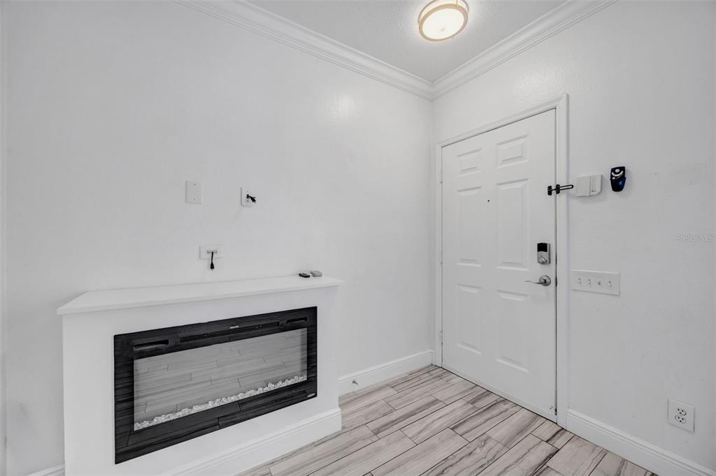 A room with white walls, wood-look tile flooring, an electric fireplace, and an entry door — 6127 BAYSIDE KEY DRIVE, TAMPA, FL