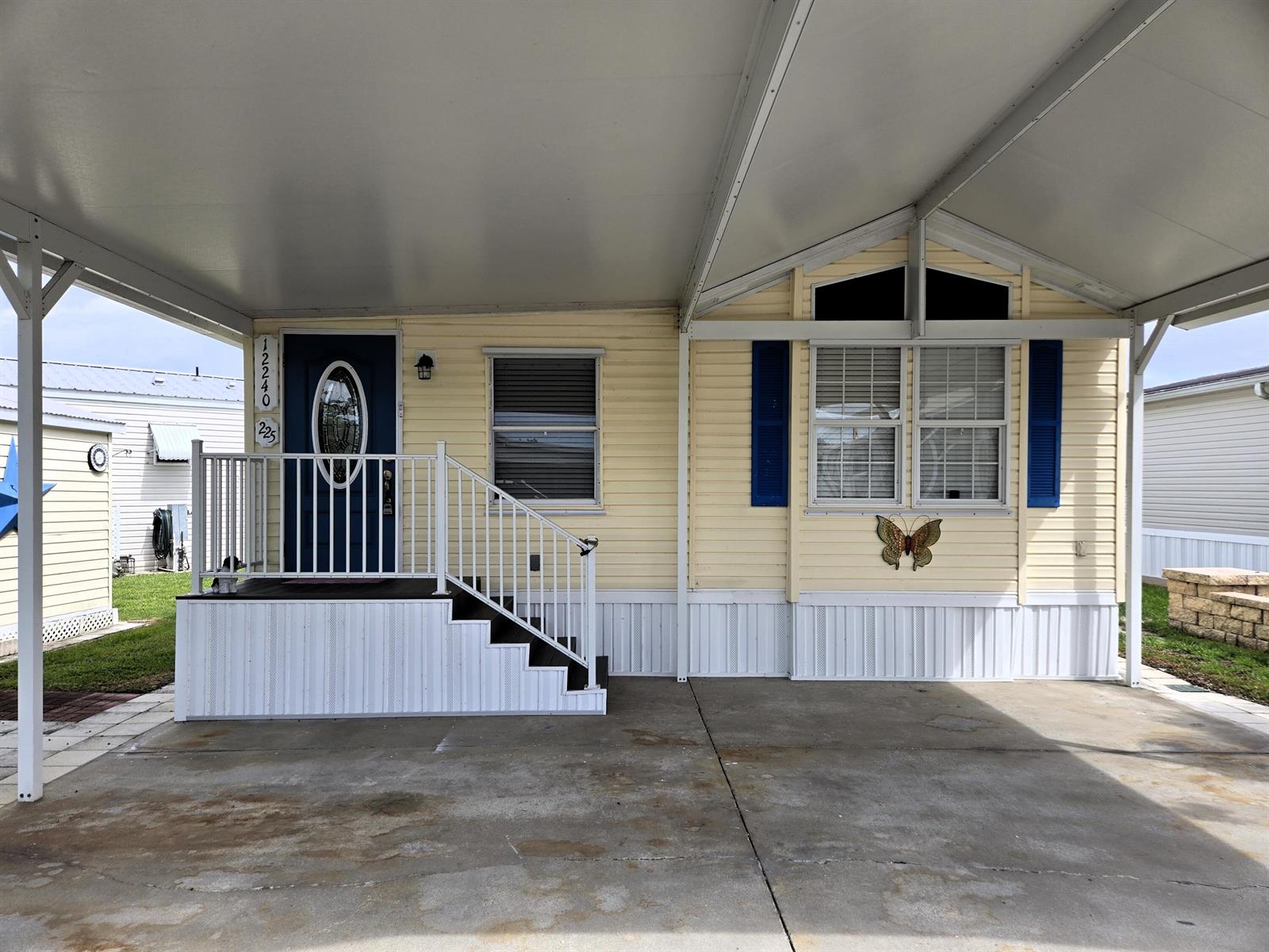 A yellow mobile home with a blue door, white railings, and a covered carport — 12240 SE 138th Boulevard # 225, Okeechobee FL 34974, OKEECHOBEE, FL