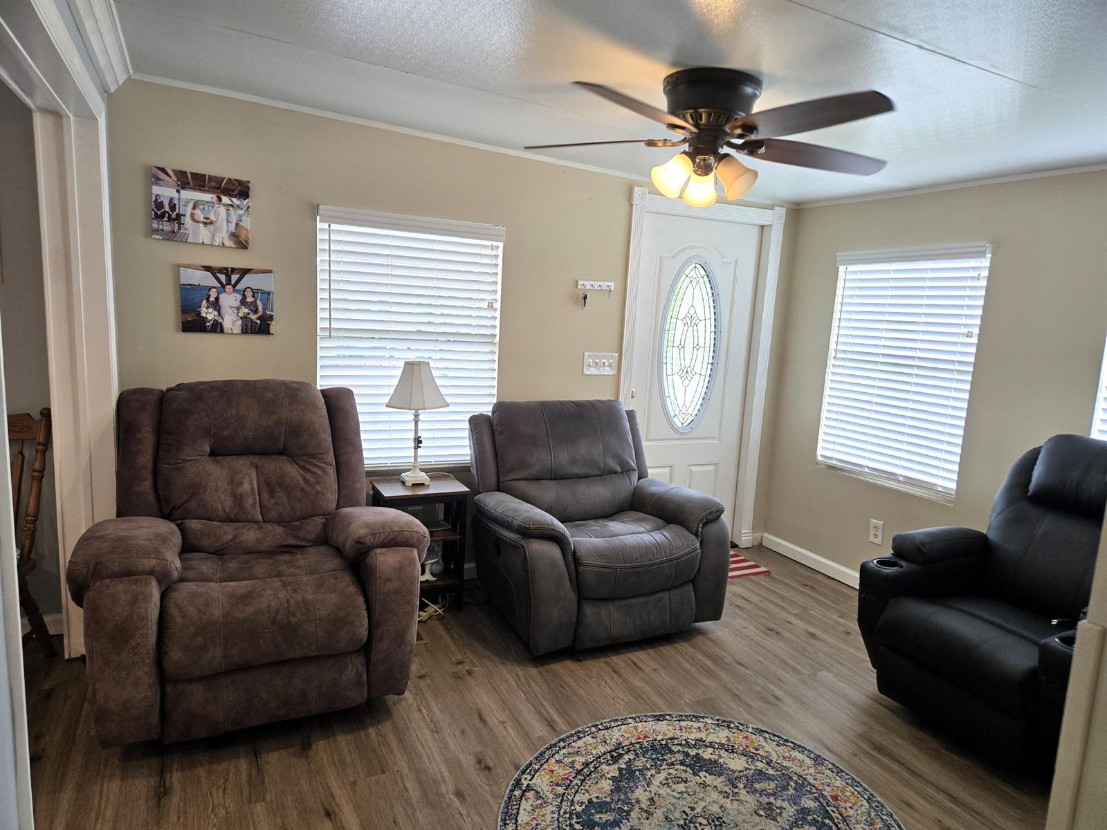 A living room features three recliners, a ceiling fan, two windows, and wood-look flooring — 12240 SE 138th Boulevard # 225, Okeechobee FL 34974, OKEECHOBEE, FL