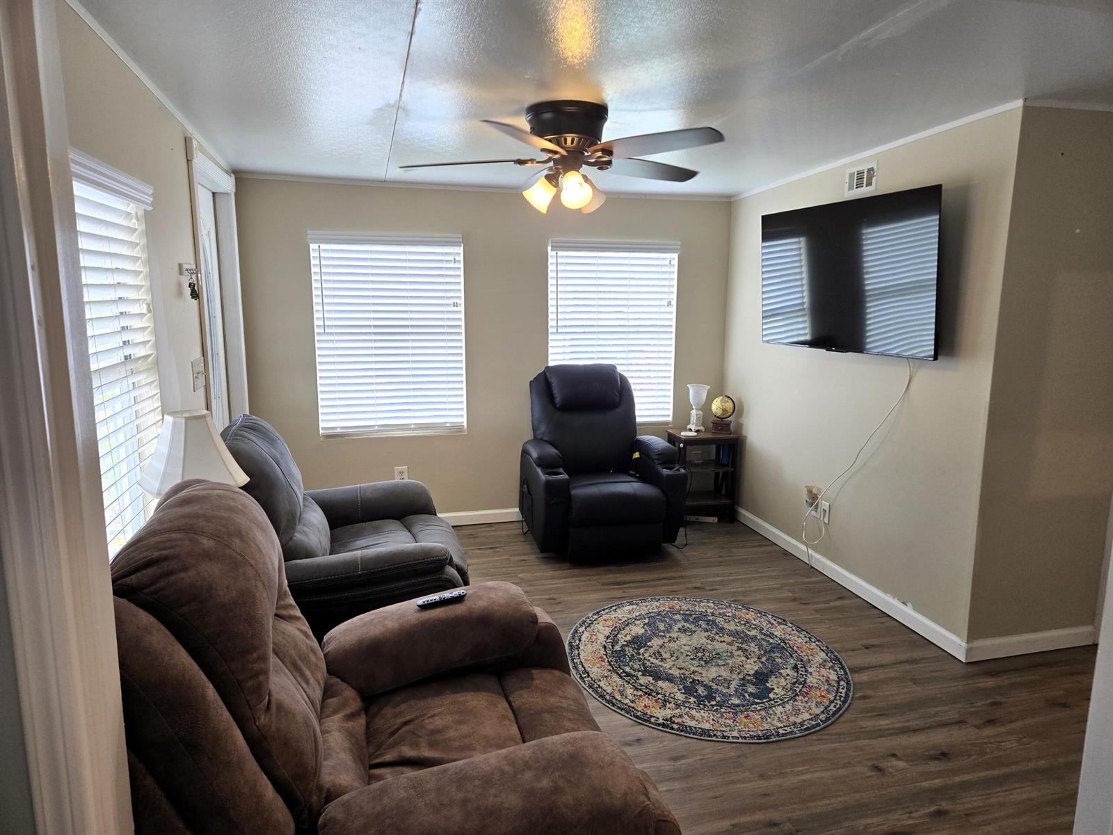 A living room features two recliners, a wall-mounted television, a ceiling fan, and wood-look flooring — 12240 SE 138th Boulevard # 225, Okeechobee FL 34974, OKEECHOBEE, FL