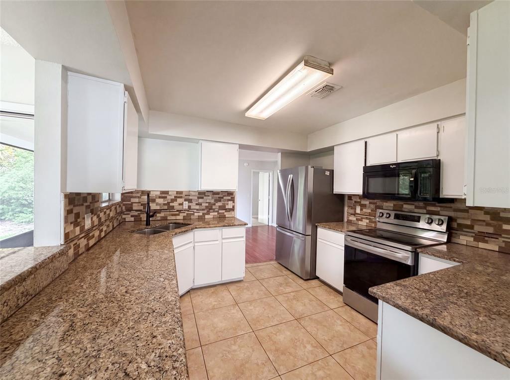 A kitchen features white cabinets, granite countertops, stainless steel appliances, and a tiled floor — 3143 BOXELDER STREET, DELTONA, FL