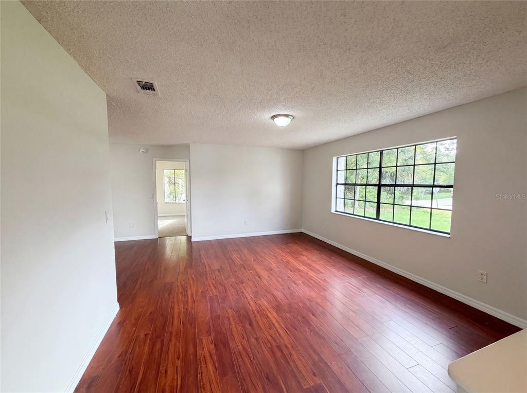 An empty room features wood-look flooring, a large window, and a textured ceiling — 3143 BOXELDER STREET, DELTONA, FL