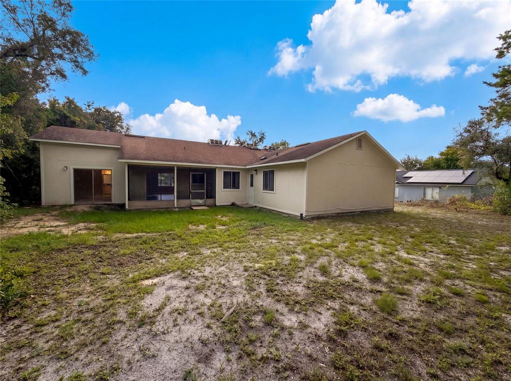 The rear exterior of a single-story house with a screened porch and a sandy yard — 3143 BOXELDER STREET, DELTONA, FL