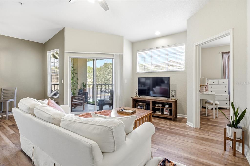 A living room features a white sofa, wood-look flooring, a television console, and a balcony — 5125 PALM SPRINGS BOULEVARD UNIT 1204, TAMPA, FL