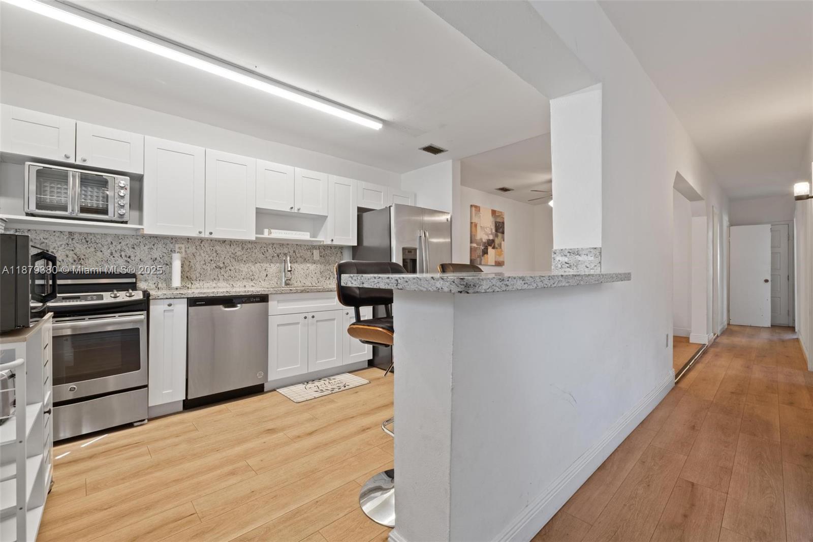A kitchen features white cabinets, stainless steel appliances, granite countertops, and light wood flooring — 2453 SW 17th St # 2453, Miami FL 33145, MIAMI, FL
