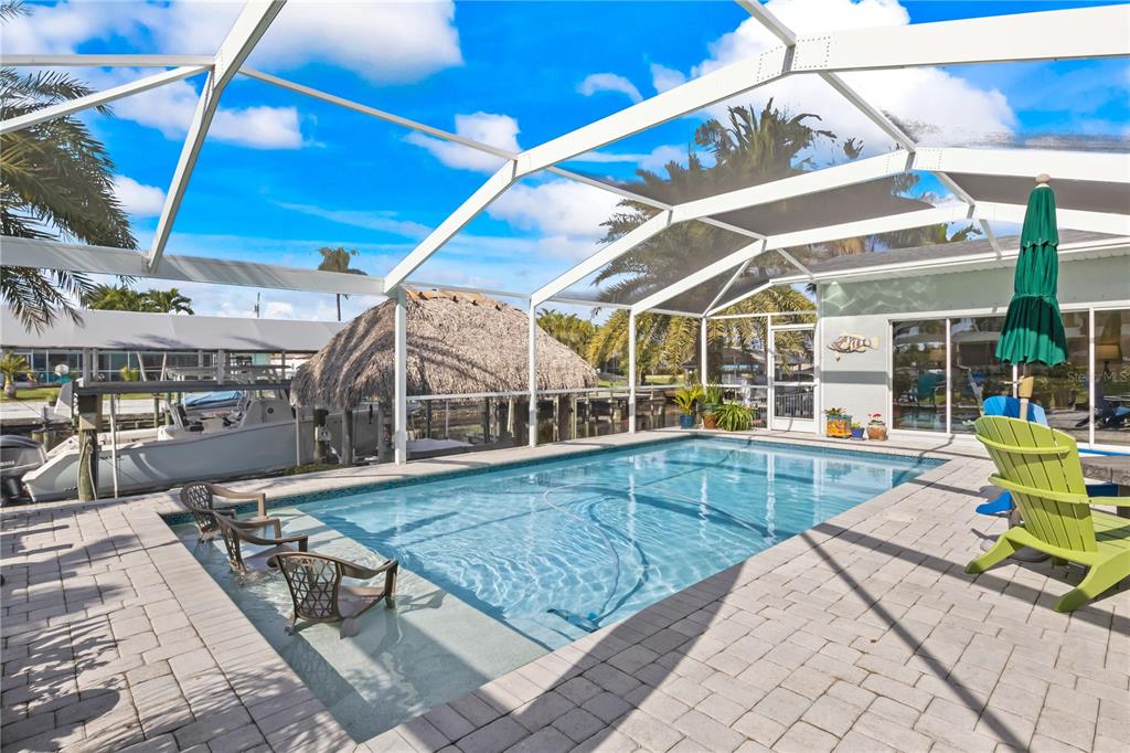 A screened-in swimming pool with a tanning ledge and patio overlooks a canal with boats — 3122 SE 18TH PLACE, CAPE CORAL, FL