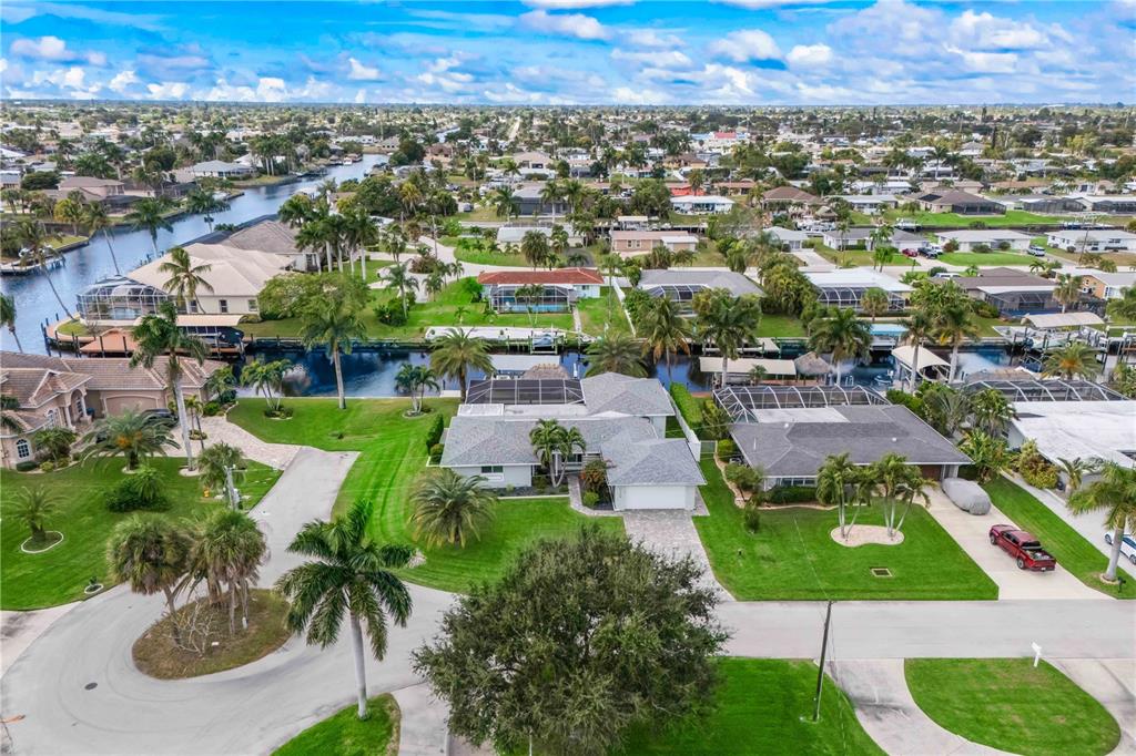 An aerial view shows a residential neighborhood with houses, palm trees, and a canal — 3122 SE 18TH PLACE, CAPE CORAL, FL