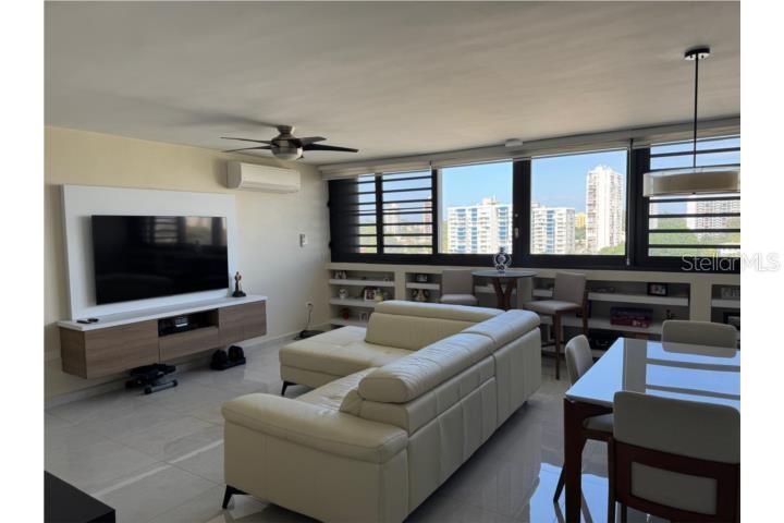 A modern living room features a white sectional sofa, a wall-mounted television, and large windows — D-10 MANSIONES DE GARDEN HILLS UNIT D-10, GUAYNABO, PR
