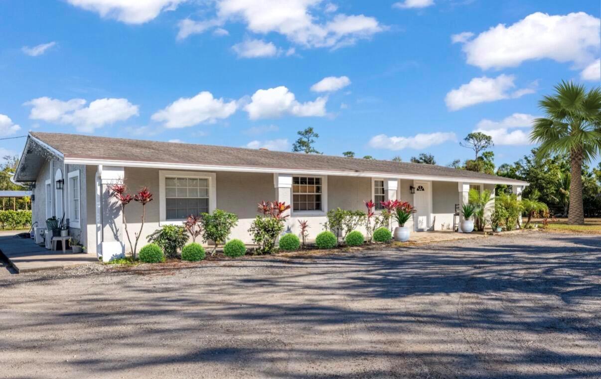 A single-story house with a gray exterior, a gravel driveway, and a palm tree — 1216 C Road, FL 33470, FL