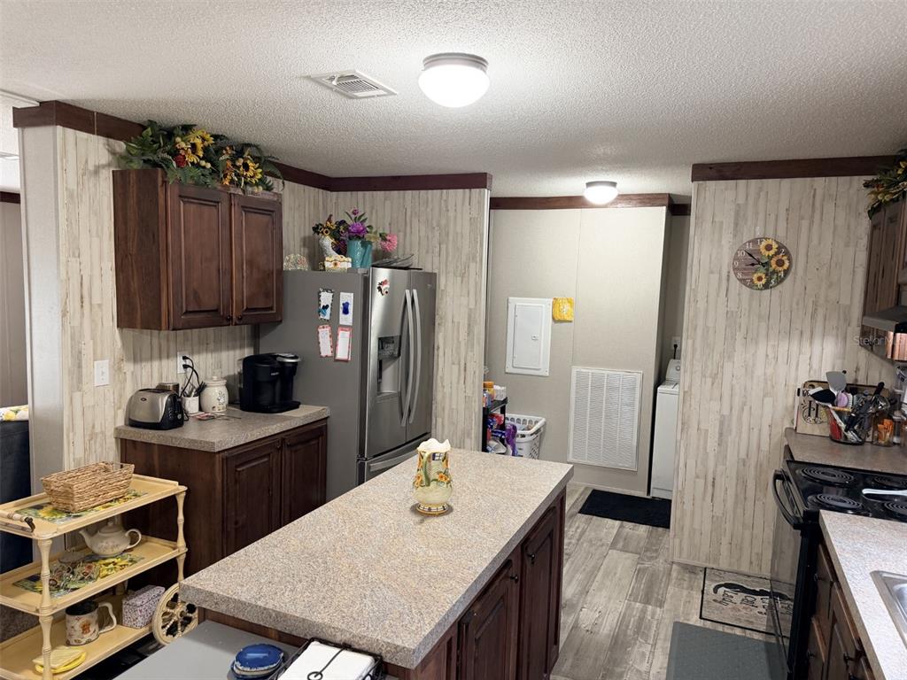 A kitchen features wood cabinets, a central island, stainless steel appliances, and light-colored wall paneling — 279 NE 576TH STREET, OLD TOWN, FL