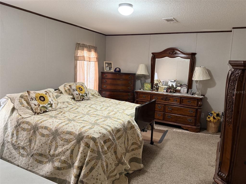 A bedroom features a bed with a patterned quilt, wooden furniture, and beige carpeting — 279 NE 576TH STREET, OLD TOWN, FL