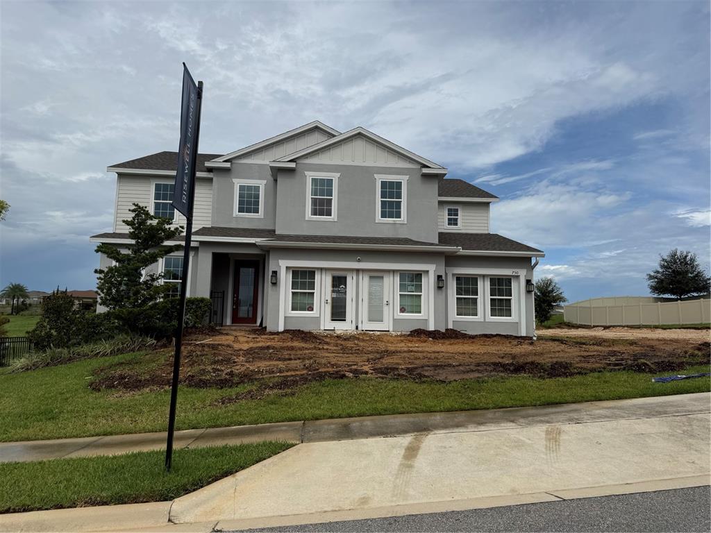A two-story gray house with a red front door and unfinished landscaping in the yard — 7504 CATANIA LOOP, CLERMONT, FL