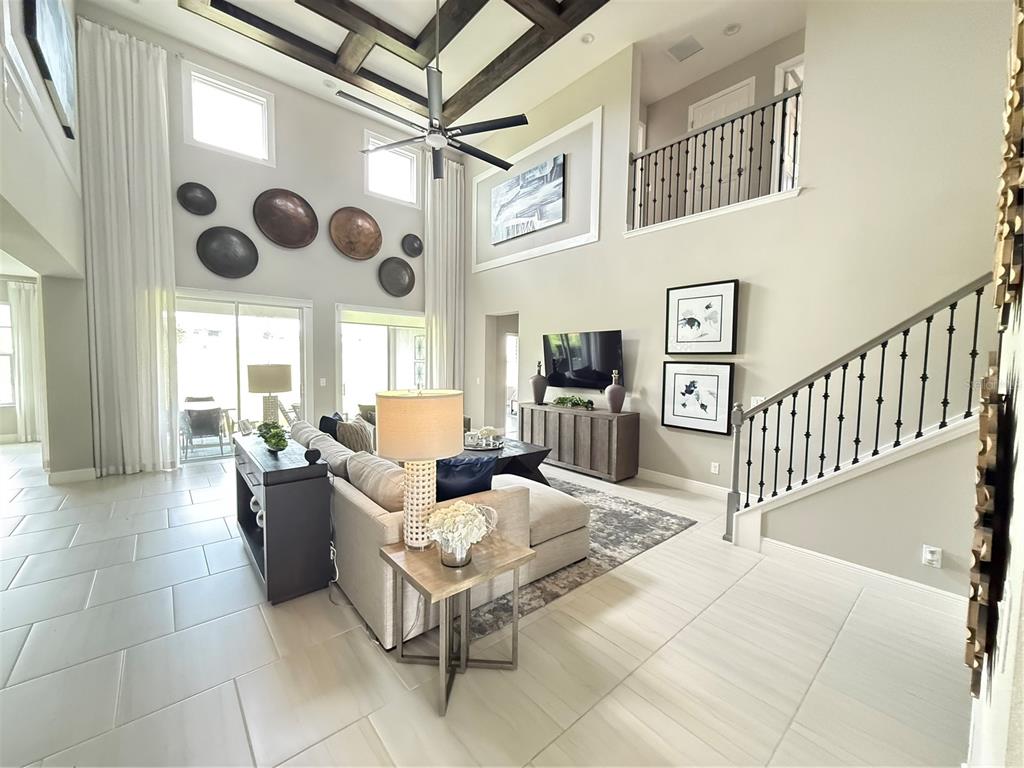 A two-story living room features a coffered ceiling, tile flooring, and a staircase — 7504 CATANIA LOOP, CLERMONT, FL