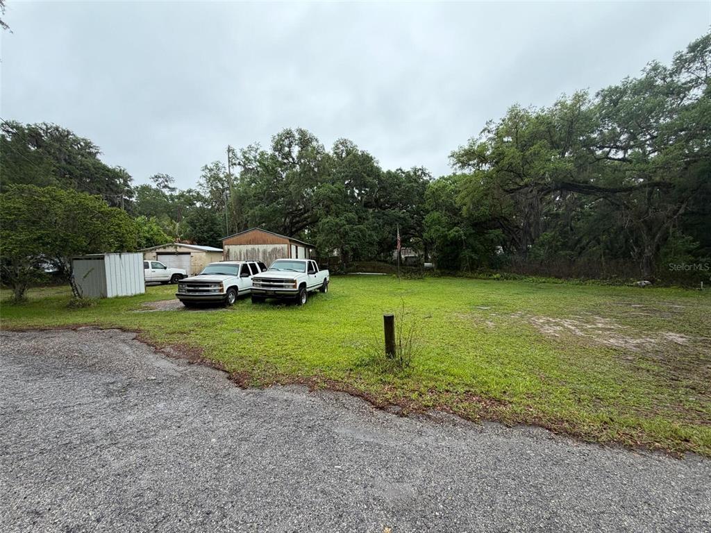 A gravel driveway leads to a grassy lot with two parked trucks and a shed — 18146 EVENING STAR AVENUE, BROOKSVILLE, FL
