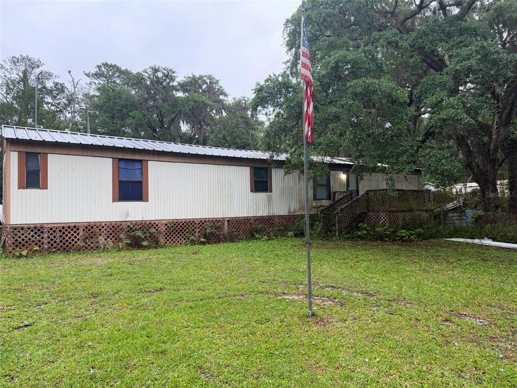 A single-story mobile home with a metal roof, lattice skirting, and a wooden deck — 18146 EVENING STAR AVENUE, BROOKSVILLE, FL