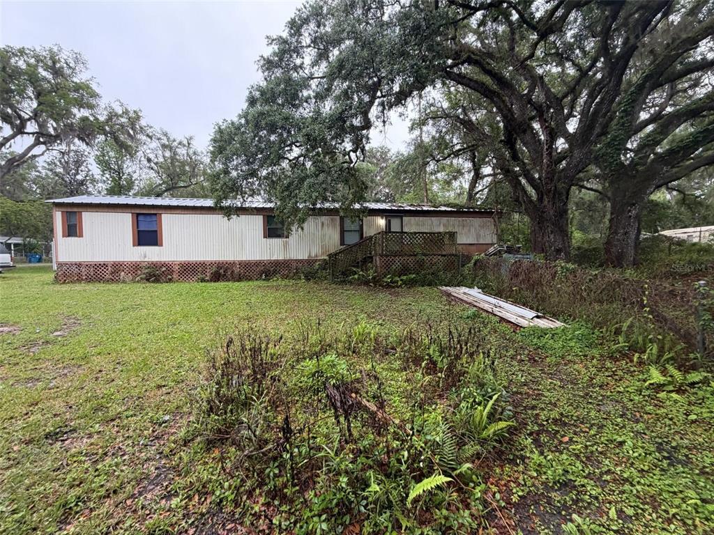 A single-story manufactured home with a wooden deck sits on a grassy lot with trees — 18146 EVENING STAR AVENUE, BROOKSVILLE, FL