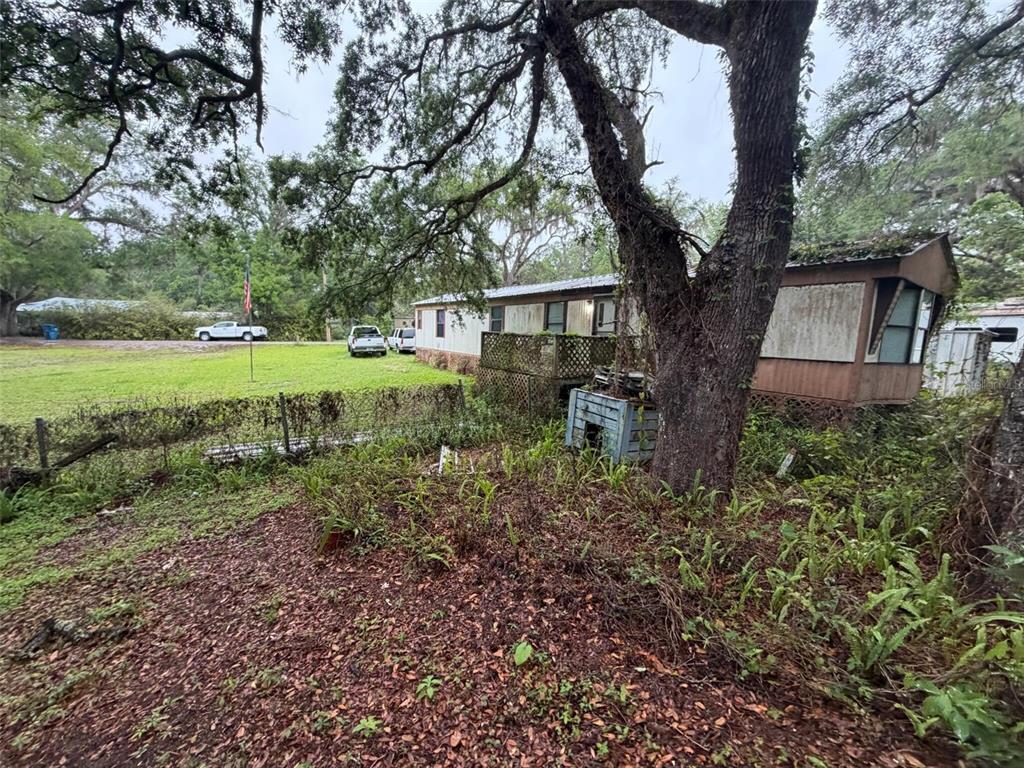 A weathered mobile home sits on a grassy lot shaded by large oak trees — 18146 EVENING STAR AVENUE, BROOKSVILLE, FL