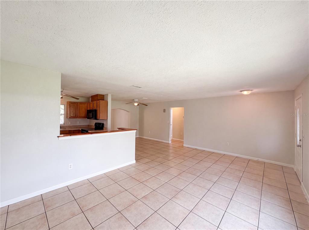 An open-concept living area with tile flooring, a kitchen pass-through, and a ceiling fan — 6309 SHERMAN TERRACE, SEBRING, FL
