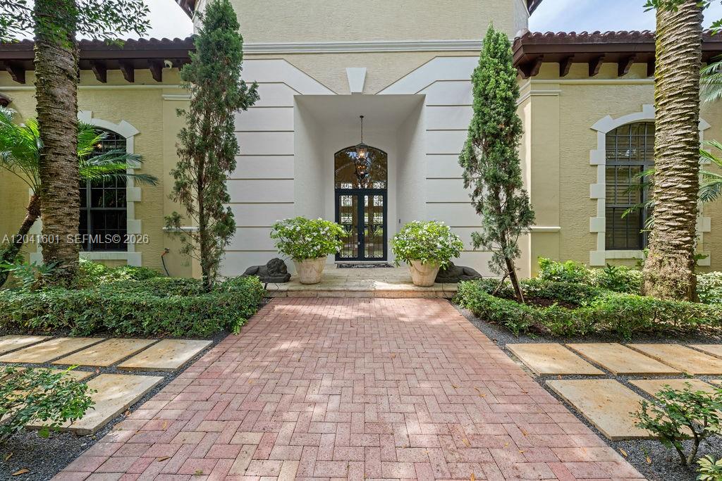 A brick walkway leads to the front entrance of a house with two potted plants — 9001 SW 59th Ct, Pinecrest FL 33156, PINECREST, FL