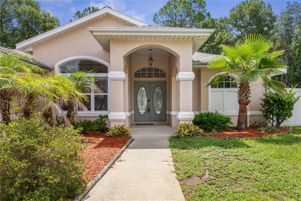 A tan single-story house with a covered entryway, double front doors, and palm trees — 137 WYNNFIELD DRIVE, PALM COAST, FL