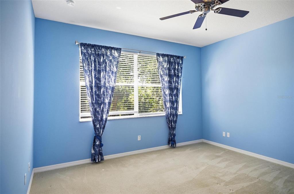 A coastal-themed bedroom features blue walls, a navy bedspread, a ceiling fan, and window curtains — 144 MENDOZA CIRCLE, DAYTONA BEACH, FL