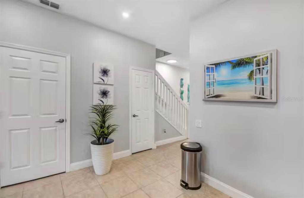 A bright entryway features light tile flooring, a staircase, two white doors, and wall art — 8117 PRINCESS PALM, KISSIMMEE, FL