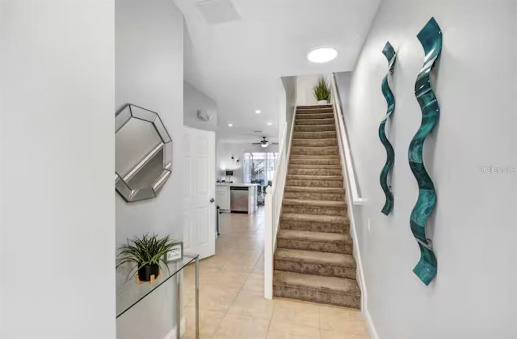 A carpeted staircase leads upward next to a tiled entryway with wall art and mirrors — 8117 PRINCESS PALM, KISSIMMEE, FL