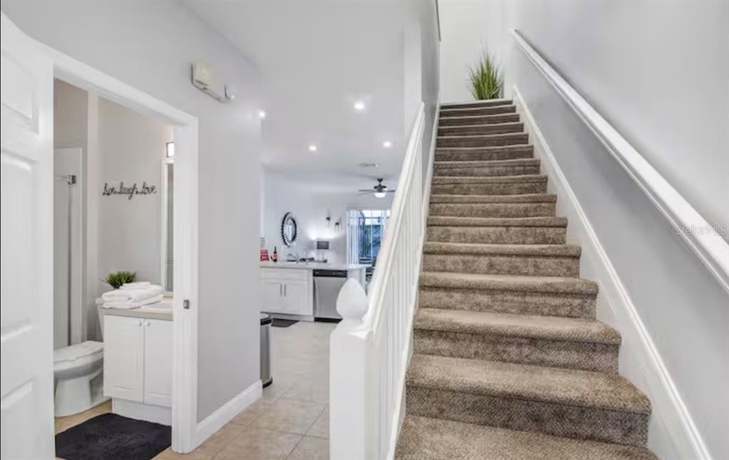 A carpeted staircase leads upstairs next to a tiled hallway with a bathroom and kitchen — 8117 PRINCESS PALM, KISSIMMEE, FL