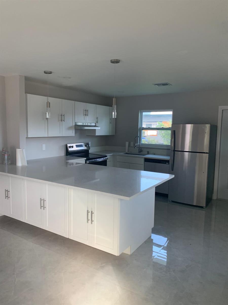 A modern kitchen features white cabinets, stainless steel appliances, and a large quartz-topped island — 3195 Mcsherry Drive S # 3195, Lake Worth FL 33461, LAKE WORTH, FL