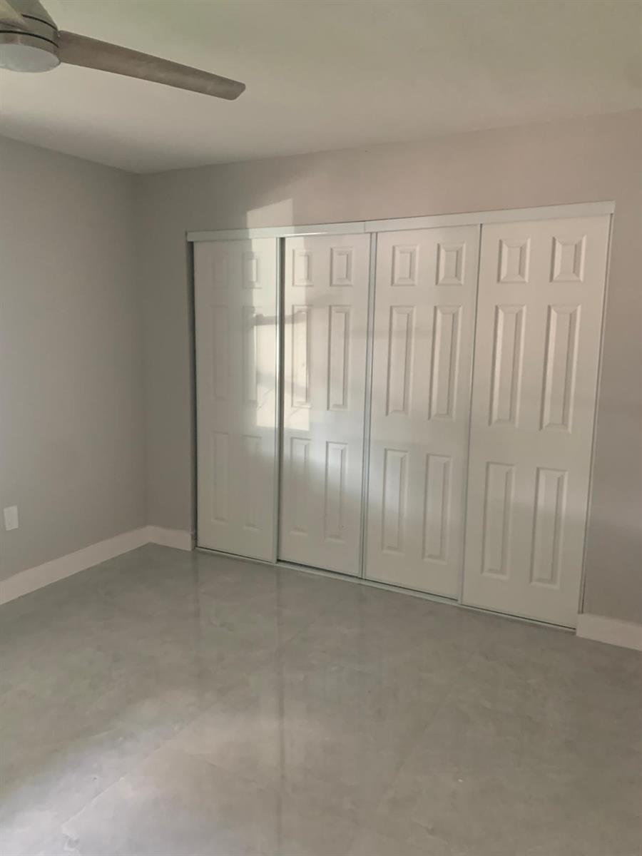 A bedroom with light gray walls, a polished concrete floor, and white sliding closet doors — 3195 Mcsherry Drive S # 3195, Lake Worth FL 33461, LAKE WORTH, FL