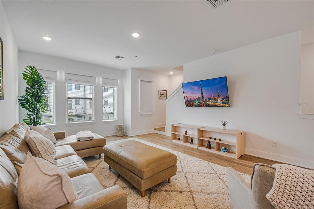 A bright living room features a leather sectional, a large ottoman, and a wall-mounted television — 12574 WILLSTATTER AVENUE, ORLANDO, FL