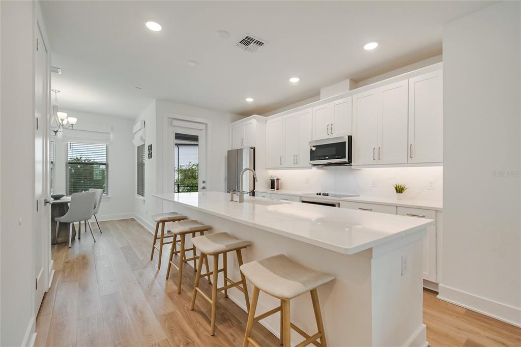 A modern kitchen features white cabinetry, a quartz island with bar stools, and light wood flooring — 12574 WILLSTATTER AVENUE, ORLANDO, FL