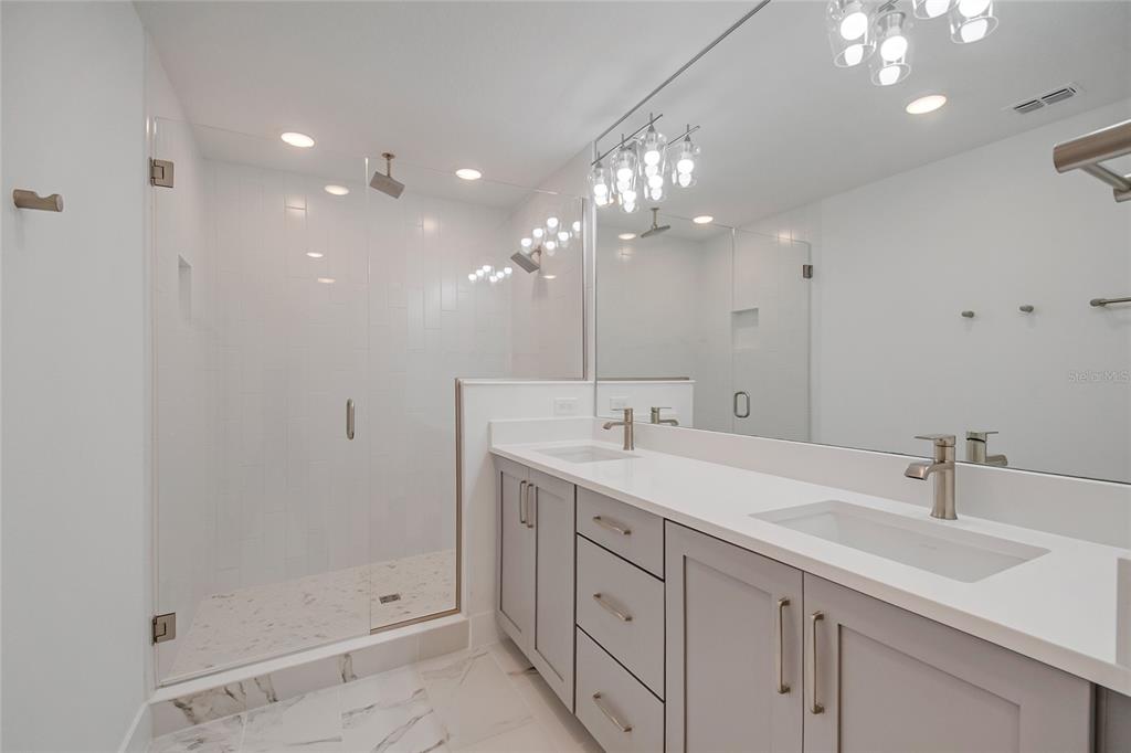 A modern bathroom features a glass-enclosed walk-in shower, double vanity with gray cabinets, and mirrors — 12574 WILLSTATTER AVENUE, ORLANDO, FL