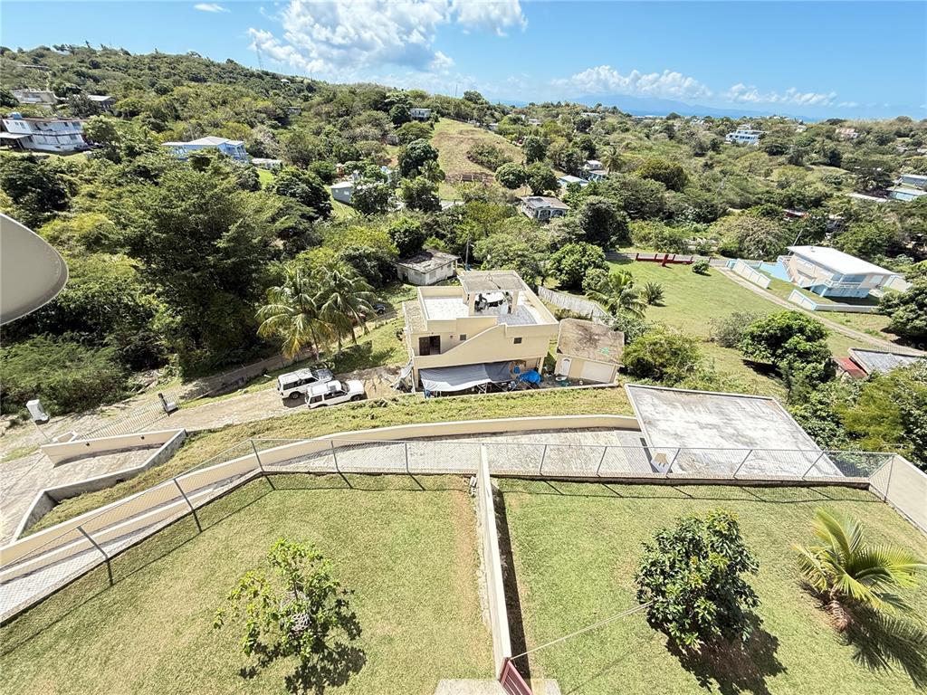 An elevated view shows a grassy yard, a multi-level house, and surrounding hills under a blue sky — Villa Borinquen BARRIO SANTA MARIA UNIT 376 & 377, VIEQUES, PR
