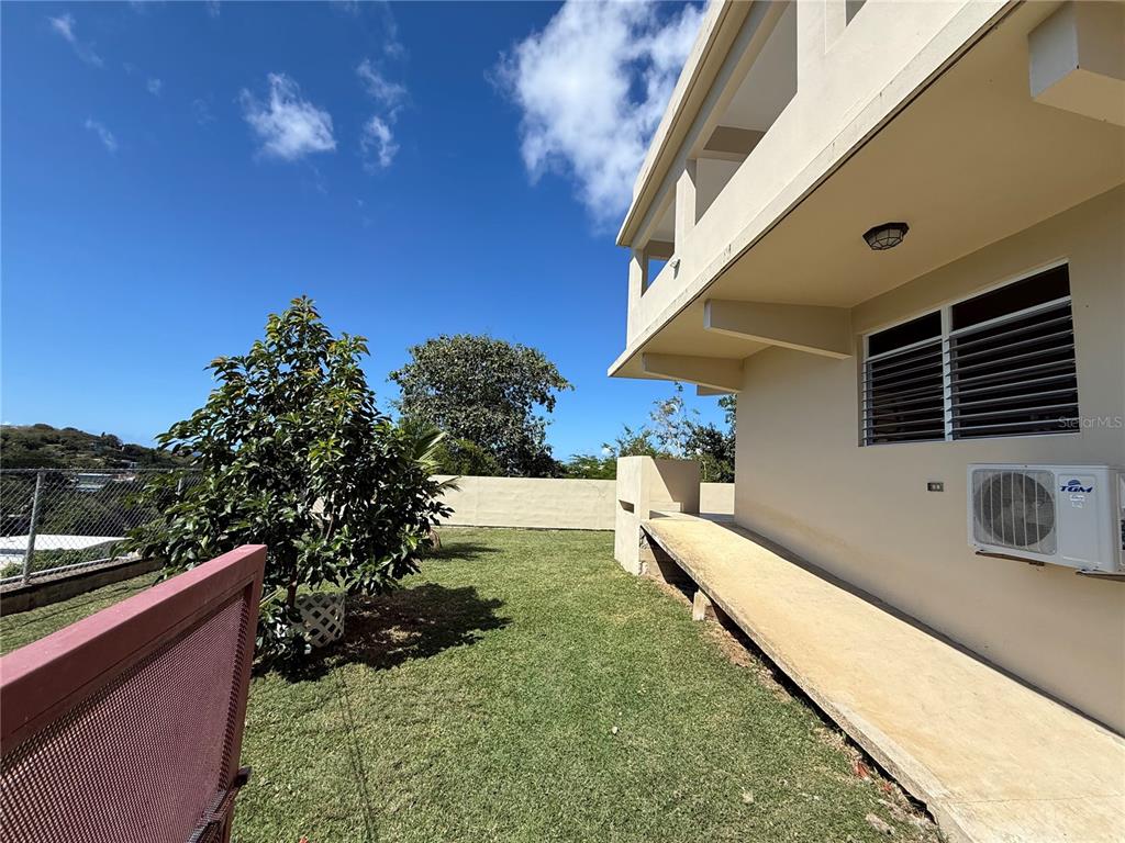 A grassy yard sits beside a beige building with a concrete walkway and air conditioner — Villa Borinquen BARRIO SANTA MARIA UNIT 376 & 377, VIEQUES, PR
