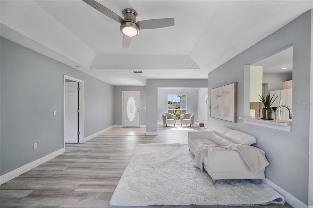 A living room features light gray walls, wood-look flooring, a white sofa, and a tray ceiling — 6059 HILLSIDE HEIGHTS DRIVE, LAKELAND, FL