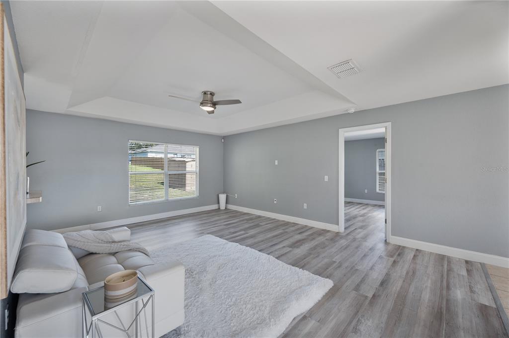 A bedroom with gray walls, wood-look flooring, a white area rug, and a tray ceiling — 6059 HILLSIDE HEIGHTS DRIVE, LAKELAND, FL