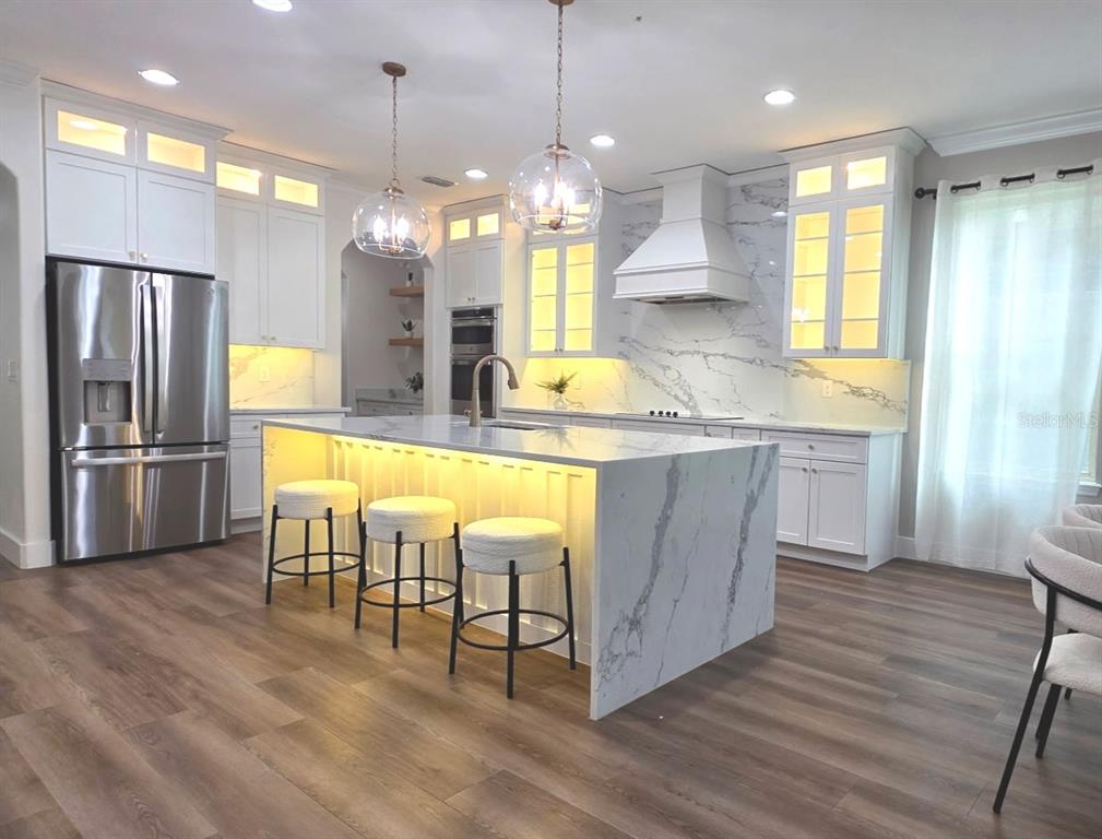 A modern kitchen features white cabinetry, a marble waterfall island, and warm under-cabinet lighting — 10169 SHALLOW WATER DRIVE, WINTER GARDEN, FL