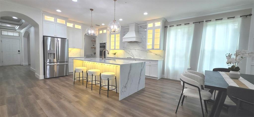 A modern kitchen features white cabinetry, a marble-topped island with stools, and wood-look flooring — 10169 SHALLOW WATER DRIVE, WINTER GARDEN, FL