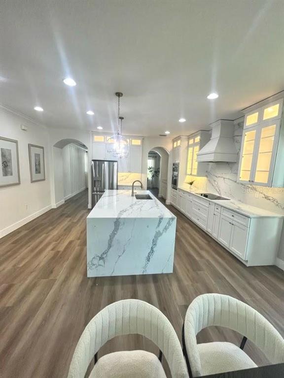 A modern kitchen features a large marble-topped island, white cabinetry, and light wood-look flooring — 10169 SHALLOW WATER DRIVE, WINTER GARDEN, FL