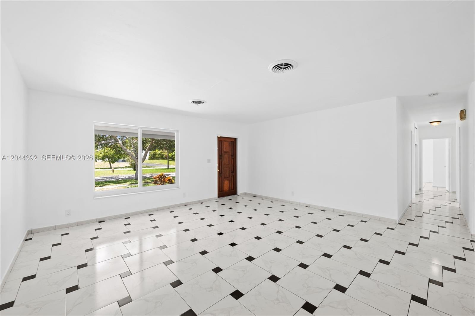 An empty room features white walls, a large window, and white tile floors with black accents — 733 N Rainbow Dr, Hollywood FL 33021, HOLLYWOOD, FL